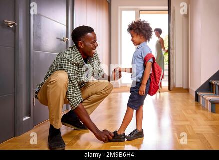 Parents à la maison aider son se préparer à aller à l'école mettre des chaussures Banque D'Images