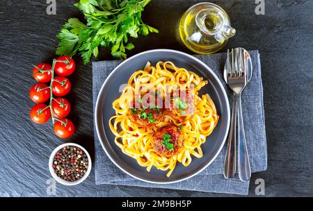 Spaghetti faits maison avec boulettes de tomate et épices servies dans une assiette grise sur fond d'ardoise noire. Pâtes cuites savoureuses avec du bœuf haché Banque D'Images