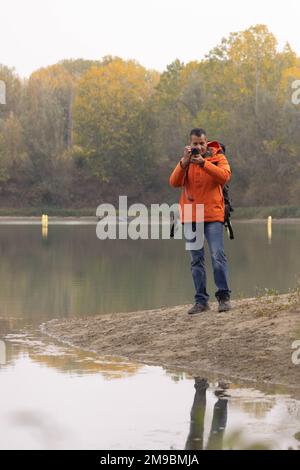 Portrait de voyageur homme au lac en automne prendre une photo avec l'appareil photo numérique et la veste orange. Photo de haute qualité Banque D'Images