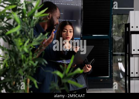 Équipe multi-ethnique de développeurs de systèmes analysant le code html sur ordinateur portable, vérifiant le projet d'intelligence artificielle. Programmeurs travaillant sur des logiciels d'apprentissage machine, développant une nouvelle interface. Banque D'Images