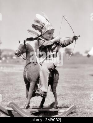 1930S GARÇON VÊTU D'UN CHAPEAU DE PLUMES D'ORIGINE AMÉRICAINE VISANT L'ARC ET LA POINTE EN CAOUTCHOUC FLÈCHE D'ÉQUITATION JOUET BERÇANT HOBBY CHEVAL PLEIN AIR - J6927 HAR001 HARS DEMI-LONGUEUR INDIENS MÂLES FLÈCHE B&W AMÉRIQUE DU NORD RÊVES AVENTURE PLUMES LOISIR ET EXCITATION RÉCRÉATION CONCEPTUEL HEADADDRESS IMAGINATION NATIVE AMÉRICAINE VISANT LA CROISSANCE JEUNES NATIFS AMÉRICAINS NOIR ET BLANC CAUCASIEN RACE PLUME BONNET HAR001 INDIGÈNE DÉMODÉE Banque D'Images