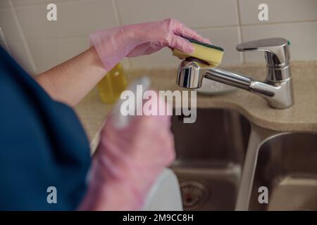 Gros plan du robinet d'eau de nettoyage des mains de housemaid avec une éponge et un spray sur la cuisine maison Banque D'Images