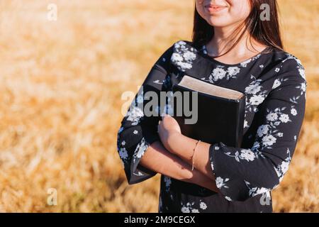 Jeune femme chrétienne méconnaissable tenant sa bible sous son bras dans le champ. Sola scriptura. Copier l'espace Banque D'Images