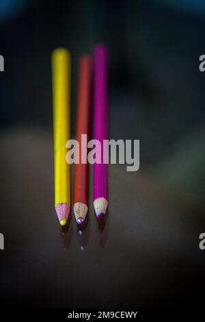 Trois crayons de couleur pointant vers l'avant sur une surface réfléchissante Banque D'Images