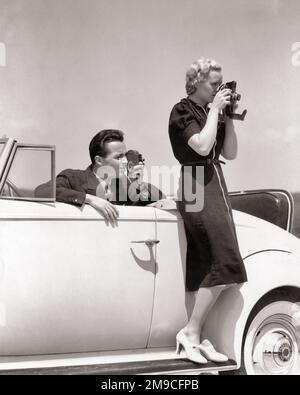 1930S HOMME DANS LE SIÈGE CONDUCTEUR D'UNE VOITURE CONVERTIBLE UTILISANT UNE CAMÉRA 8MM BLONDE FEMME DEBOUT SUR LA COURSE À PIED UTILISANT APPAREIL PHOTO - M5568 HAR001 HARS STYLE DE SIÈGE PHOTOGRAPHE COMMUNICATION VÉHICULE JEUNE ADULTE TRAVAIL D'ÉQUIPE INFORMATION VACANCES DÉTENTE STYLE DE VIE FEMMES MARIÉES ÉVÉNEMENT RURAL CONJOINT ÉPOUX LUXE COPIE ESPACE AMITIÉ PLEINE LONGUEUR DAMES PERSONNES AUTOMOBILE MÂLES CONFIANCE TRANSPORT SPECTATEURS B&W PARTENAIRE TEMPS DE REPOS COMPÉTENCE ACTIVITÉ AMUSEMENT TÊTE ET ÉPAULES AVENTURE HOBBY STYLES VOYAGE INTÉRÊT AUTOS ESCAPADE HOBBIES SAVOIR PASSE-TEMPS PLAISIR VACANCES EN UTILISANT DES AUTOMOBILES ÉLÉGANT Banque D'Images