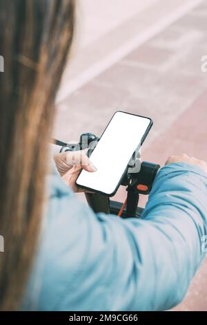 vue arrière supérieure de la latina, femme à bord d'un scooter électrique avec smartphone Banque D'Images