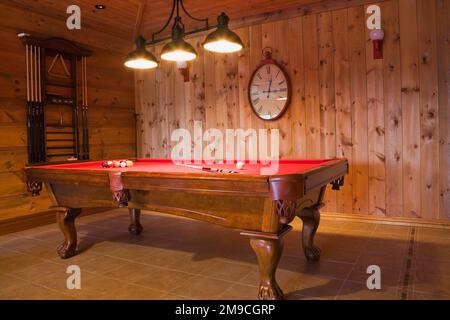 Pied à griffes en bois avec table de billard en feutre rouge dans la salle de jeux adjacente à la salle familiale au rez-de-chaussée à l'intérieur d'un profil en rondins plat et d'une maison en bois. Banque D'Images