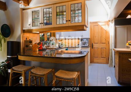 Cuisine avec armoires en verre en bois blanc et bar avec tabourets de bar et comptoirs en granit noir à l'intérieur de la maison en rondins de style Canadiana. Banque D'Images