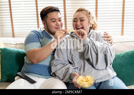 Un jeune couple asiatique de chubby regarde une série télévisée et un film sur le canapé dans le salon. Homme et femme qui s'amusent ensemble à la maison. Les gens rient et sourient ensemble Banque D'Images
