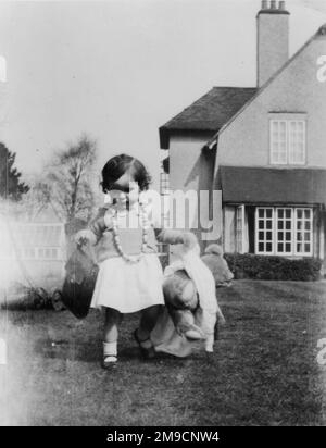 Une petite fille dans le jardin arrière d'une maison à Fleet, Hampshire. Elle porte un étui pour appareil photo dans une main et son ours en peluche dans l'autre. Banque D'Images