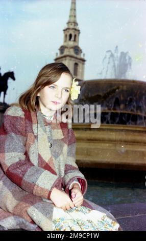 Une petite fille est assise à Trafalgar Square, dans le centre de Londres, avec une fontaine et la flèche de Saint Martin dans les champs derrière elle. Banque D'Images