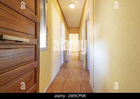 Hall d'entrée avec porte lambrissée en bois d'une maison vide avec un long couloir menant à plusieurs chambres et fenêtres Banque D'Images