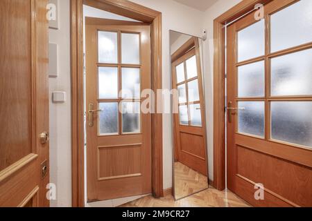 Hall d'entrée d'une maison avec portes en chêne et accès à plusieurs chambres avec portes du même matériau avec des fenêtres et un miroir incliné sur le mur Banque D'Images