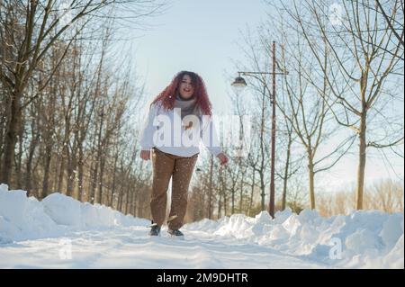 Femme souriante à tête rouge en train de courir au parc en hiver. Banque D'Images