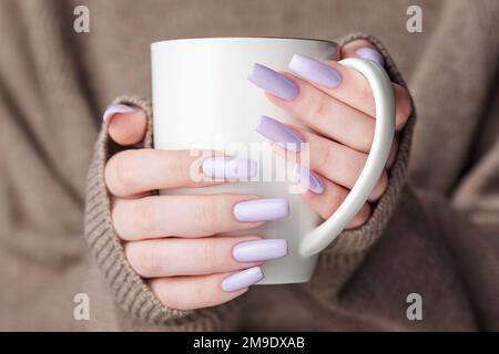 Manucure féminine tendance. Mains de femme avec manucure violette tenant une tasse de thé. Concept d'hiver ou d'automne confortable. Banque D'Images