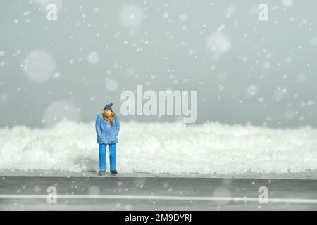 Photographie miniature de personnage de jouet de personnes. Problème de transport pendant l'hiver. Un homme qui attend sur une route vide pendant une tempête de neige. Photo d'image Banque D'Images