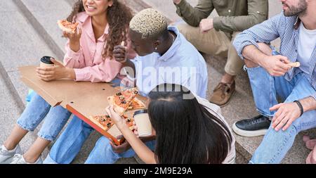 des étudiants affamés qui dégusteraient une délicieuse pizza sur les marches. vue de dessus. Banque D'Images