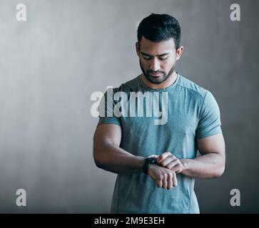 Ce pourrait être un nouveau meilleur personnel. un jeune athlète masculin élégant qui vérifie sa montre intelligente sur fond gris. Banque D'Images