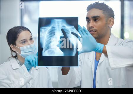 La maladie vient d'ici. deux médecins analysant une radiographie ensemble dans un hôpital. Banque D'Images