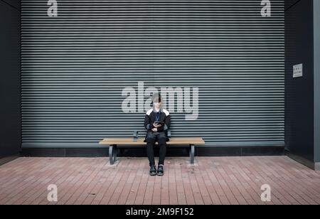 Tokyo- Japon- Circa novembre 2018. Un jeune solitaire en interaction avec un smartphone contre un obturateur fermé . Concept de solitude. Banque D'Images