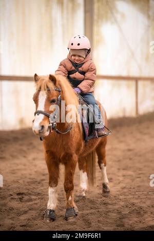 Leçon de équitation pour les petits enfants. Une jeune fille de trois ans fait du poney et fait des exercices Banque D'Images