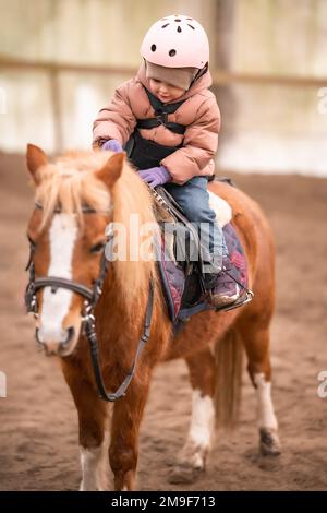 Leçon de équitation pour les petits enfants. Une jeune fille de trois ans fait du poney et fait des exercices Banque D'Images