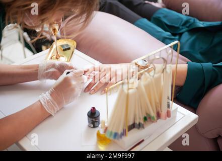 Manucure professionnelle faisant manucure pour femme client dans le salon de beauté. Gros plan du spécialiste de la manucure en gants stériles appliquant du vernis à ongles rouge sur l'ongle de la femme. Banque D'Images