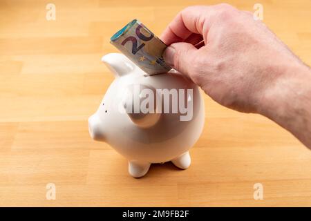 La main met 20 euros de facture dans la banque de piggy Banque D'Images