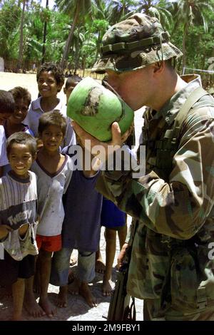 LE caporal GREGORY Hughes, un SAW (arme automatique Squad) GUNNER avec le troisième peloton, Compagnie de l'Inde, Bataillon Landing Team 3/1, 13th Marine Expeditionary Unit (Special Operations ALEGCE), s'arrête pour une boisson rafraîchissante d'une noix de coco que les enfants locaux ont offert avec gratitude lors d'une opération d'assistance humanitaire, Timor oriental, Septembre 2000. LES marins AMÉRICAINS et les marins du Tarawa Amphiobie Ready Group ont passé trois jours au Timor oriental à fournir des services de relations médicales et communautaires pour aider à reconstruire la nation déchirée par la guerre. Objet opération/série: ASSISTANCE HUMANITAIRE OPERATI Banque D'Images