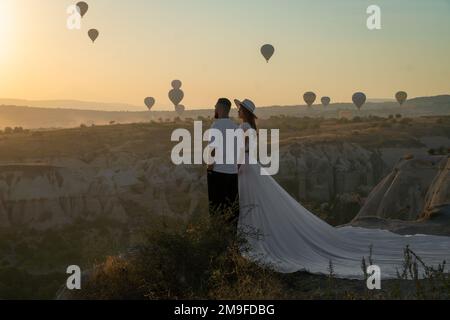 Cappadoce, Turquie-20 septembre 2022: Beau couple élégant dans l'amour se tient contre le fond des ballons à l'aube et tient les mains. Banque D'Images