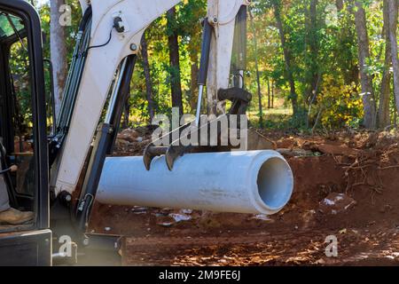 Le travailleur utilise le tracteur pour soulever les tuyaux d'égout en béton du sol en vue de leur installation souterraine Banque D'Images