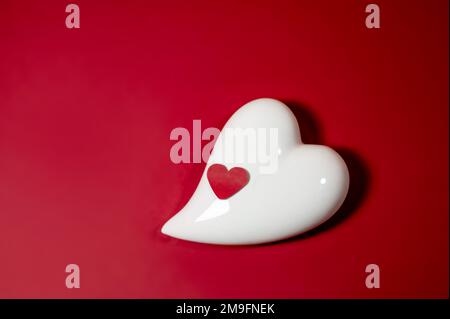 Coeur en porcelaine blanche et petit coeur en papier sur fond rouge, symbole d'amour et carte de vœux pour des vacances comme la Saint Valentin ou la fête des mères, espace de copie Banque D'Images