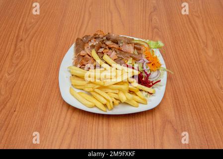 Un grand plat de kebab de pommes de terre frites avec salade et mélange de poulet et de viande d'agneau sur une table en merisier et un plat blanc Banque D'Images