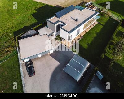 Vue aérienne de la maison moderne dans la campagne avec une grande place de parking et des panneaux solaires sur le toit plat Banque D'Images