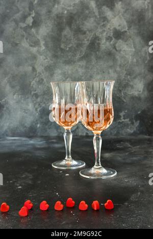 Gros plan sur deux verres de liqueur et petits coeurs rouges, fond noir Banque D'Images