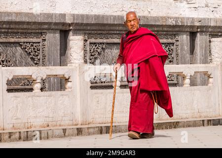 Moine tibétain en robe rouge avec promenades en bâton le long d'un mur décoré de Kumbum Champa Ling Monastère, Xining, Chine Banque D'Images