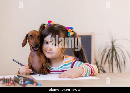 adorable petite fille tire avec son ami chien dachshund. Enfants et animaux. Chiens acceptés Banque D'Images