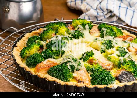 Vue en gros plan de délicieux brocoli et quiche de saumon fraîchement cuits sur la grille de refroidissement sur une table en bois. Banque D'Images