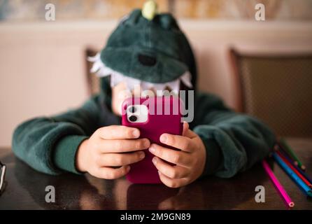 Gros plan portrait d'un garçon qui regarde dans le téléphone assis sur le sol, le téléphone se recharge Banque D'Images