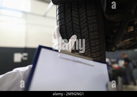 Le technicien mécanicien d'automobiles tient une feuille de presse-papiers vierge à portée de main avec le texte de l'espace de copie et les pneus de voiture Banque D'Images