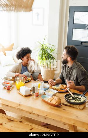 Vue panoramique sur les jeunes couples biraciaux qui parlent et qui ont le petit déjeuner tout en étant assis à la table à manger Banque D'Images