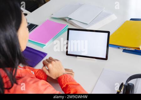 Image d'une femme biraciale utilisant une tablette avec un espace de copie à l'écran assis au bureau Banque D'Images