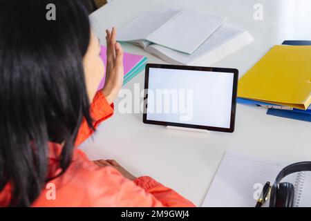 Image d'une femme biraciale utilisant une tablette avec un espace de copie à l'écran assis au bureau Banque D'Images