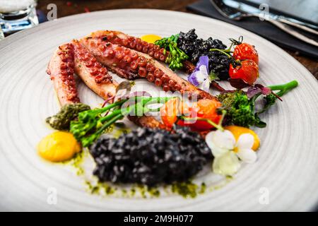 Poulpe avec risotto noir. Crème de carottes, mini-brocoli, pesto de basilic. Une délicieuse cuisine traditionnelle saine est servie pour le déjeuner dans une cuisine gastronomique moderne Banque D'Images