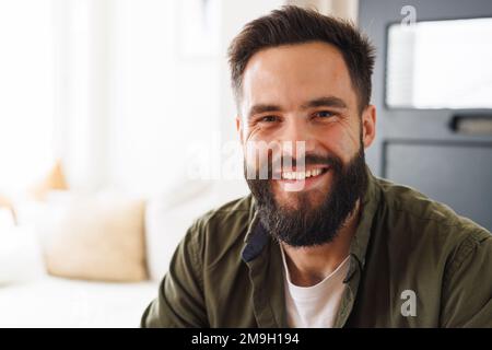 Portrait en gros plan d'un jeune homme souriant biracial barbu portant une veste dans le salon, espace copie Banque D'Images