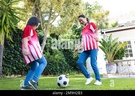 Bonne mère asiatique et fille jouant au football ensemble dans le jardin Banque D'Images