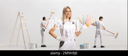 Femme peintre de maison tenant une palette de nuances de couleur et ouvriers masculins peignant un mur Banque D'Images