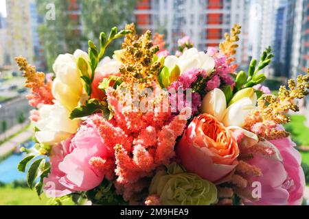 Bouquet coloré de pivoines, astilbe, freesia, roses de pivoines Juliette, limonium, dianthus et Pittosporum verdure sur le bord de la fenêtre de l'appartement de la ville. Banque D'Images