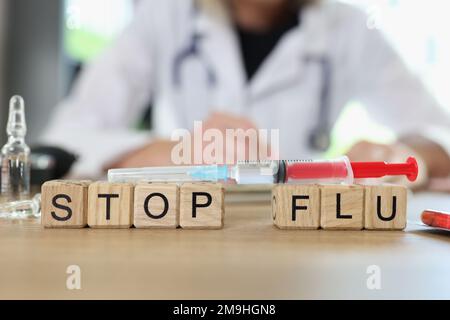Arrêter les mots sur la grippe sur les cubes en bois et la seringue de vaccin sur la table, médecin en arrière-plan. Banque D'Images
