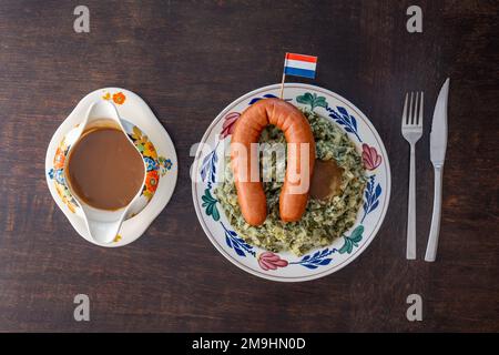 Portion de pommes de terre traditionnelles hollandaises « Boerenkool Stamppot met Mpires » écrasées avec du chou frisé, de la saucisse fumée et de la sauce sur une assiette avec drapeau hollandais Banque D'Images